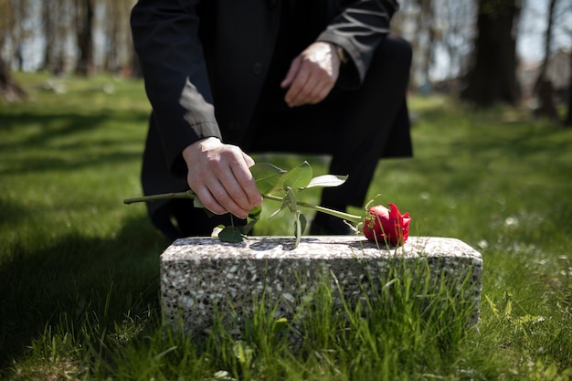 Man bringing a rose to a tombstone at the cemetery